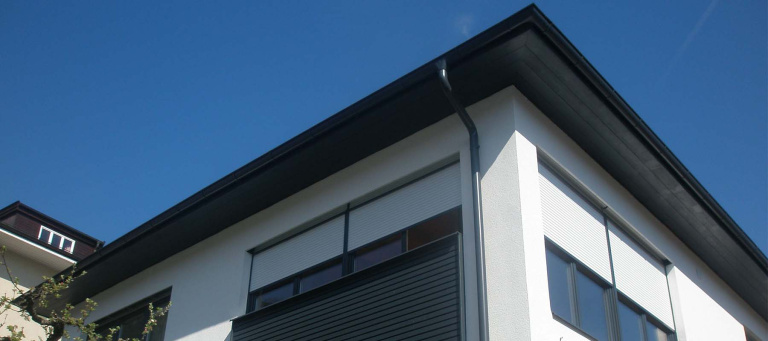 Moderne Hausansicht mit flachem Dach und großen Fenstern in strahlendem Blau.