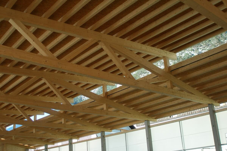 Holzkonstruktion mit sichtbaren Balken und Fachwerk unter einem lichtdurchfluteten Dach.
