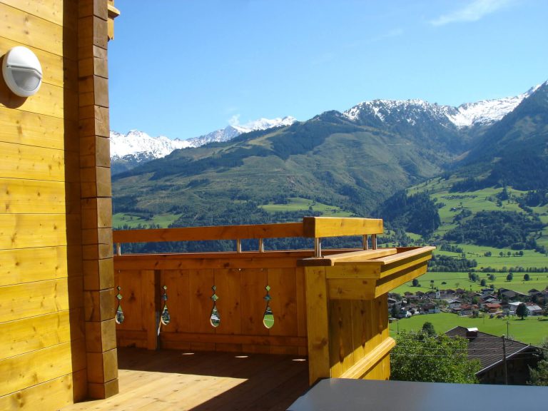 Holzbalkon mit Blick auf die Berge und das grüne Tal im Pinzgau bei klarem Himmel.