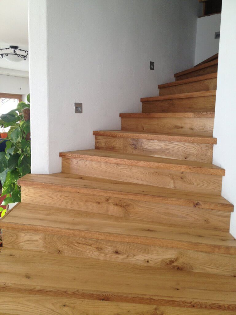 Helle Holztreppe mit breiten Stufen in modernem Innenraum und Pflanzen dekoriert.