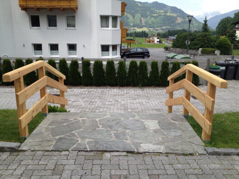 Holzbrücke über einen Steg mit Steinboden in einer Wohngegend in Piesendorf.