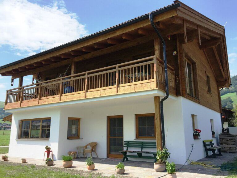 Holzhaus mit Balkon und Blumen, umgeben von grüner Landschaft in Piesendorf.