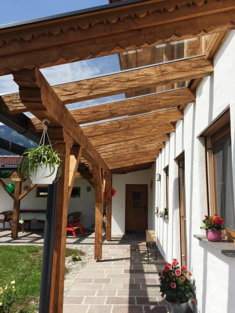 Holzterrasse vor einem modernen Wohnhaus mit begrünten Blumenkübeln und rustikalen Elementen.