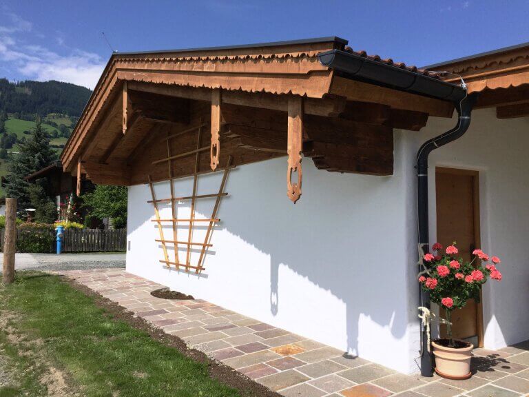 Holzfassade mit geschwungenem Dachvorsprung und blühenden Rosen in Piesendorf.