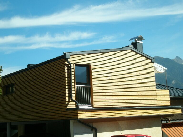 Moderne Holzkonstruktion mit Fenster und Balkon im Pinzgau, umgeben von Bergen.