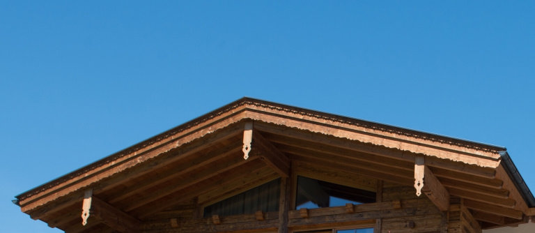 Detailansicht eines Holzhausdaches mit Holzverzierungen unter klarem Himmel.