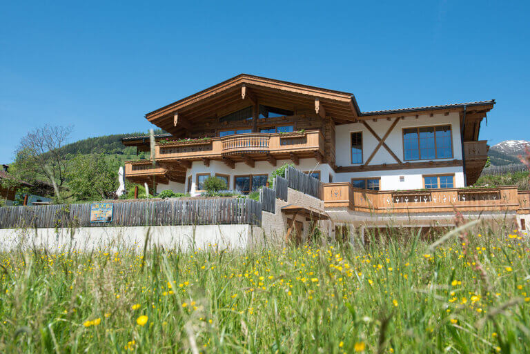 Moderne Holzbau-Villa in Piesendorf, umgeben von Wiese und Bergen, mit eleganter Terrasse.